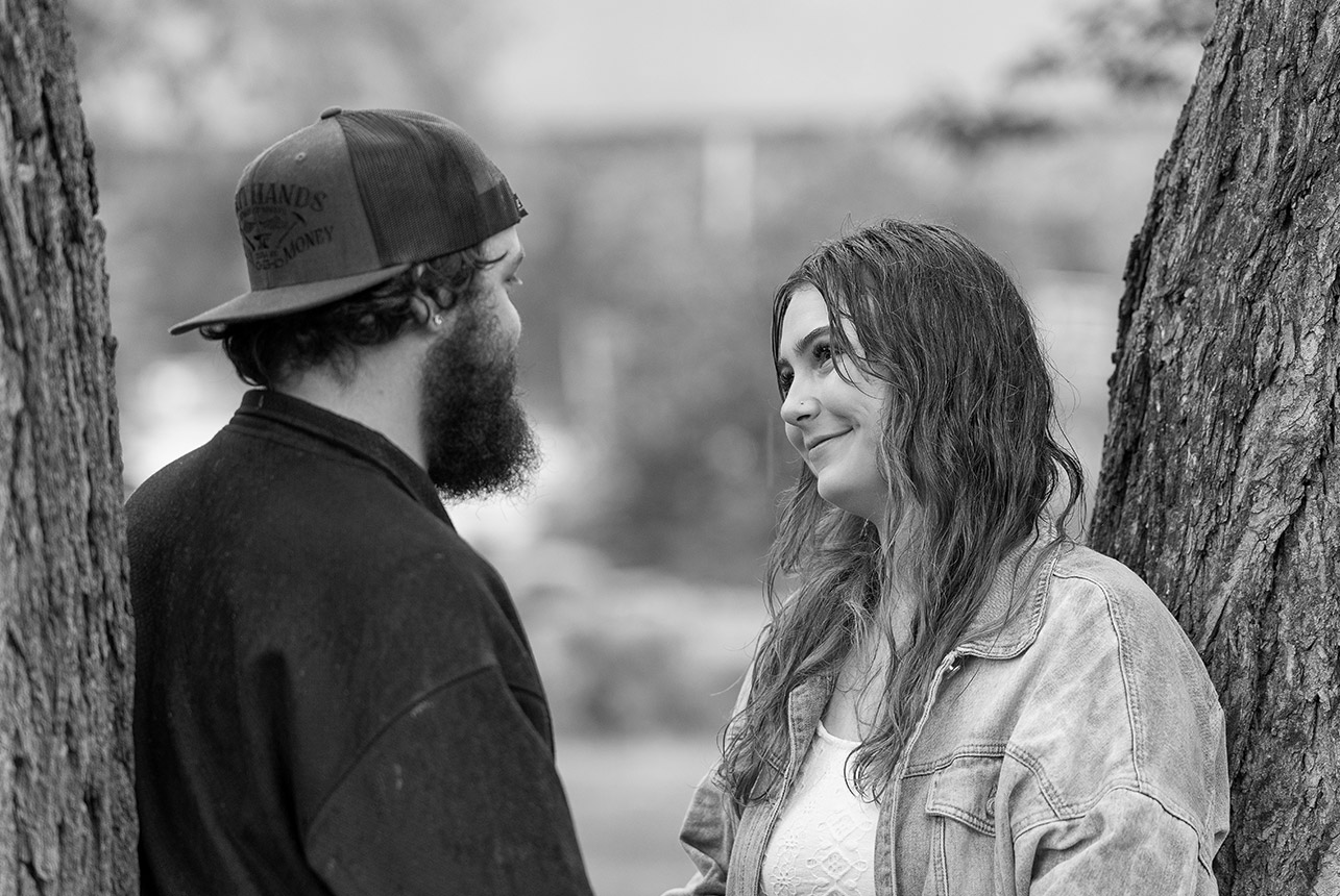 Woman smiles at her partner while standing between trees during a black and white engagement session