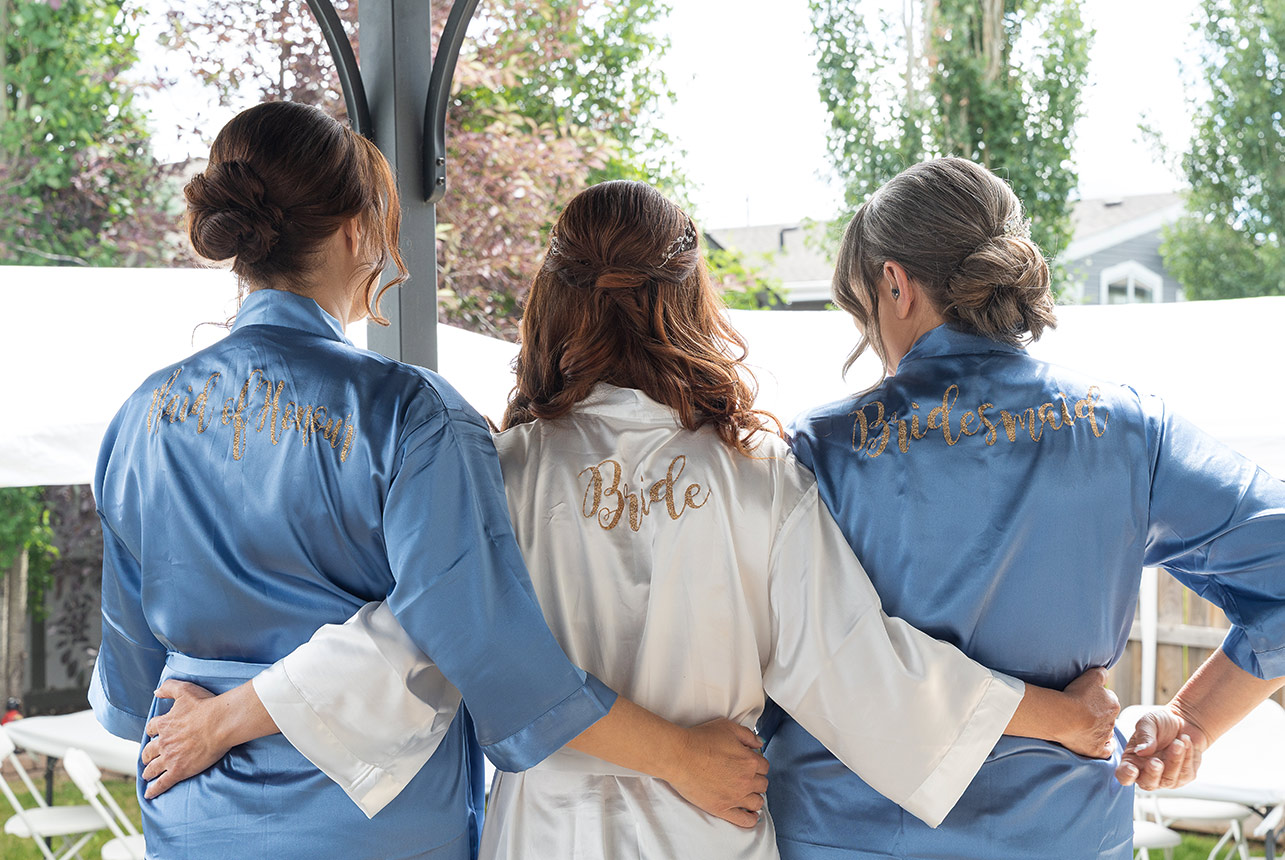 Bride and bridesmaids in satin robes with gold lettering before wedding