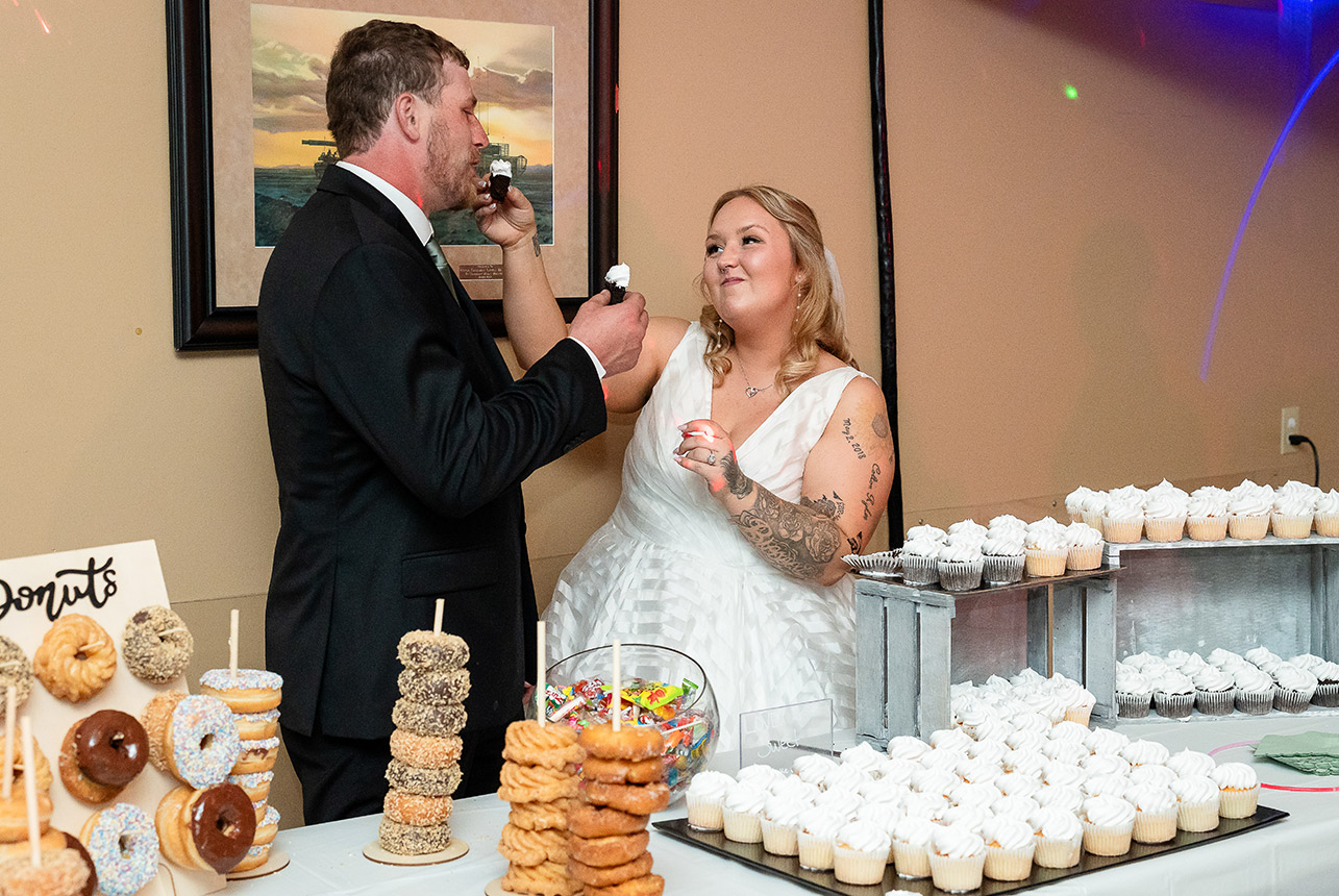 Bride and groom share a playful moment as they cut a cupcake in half during their wedding reception