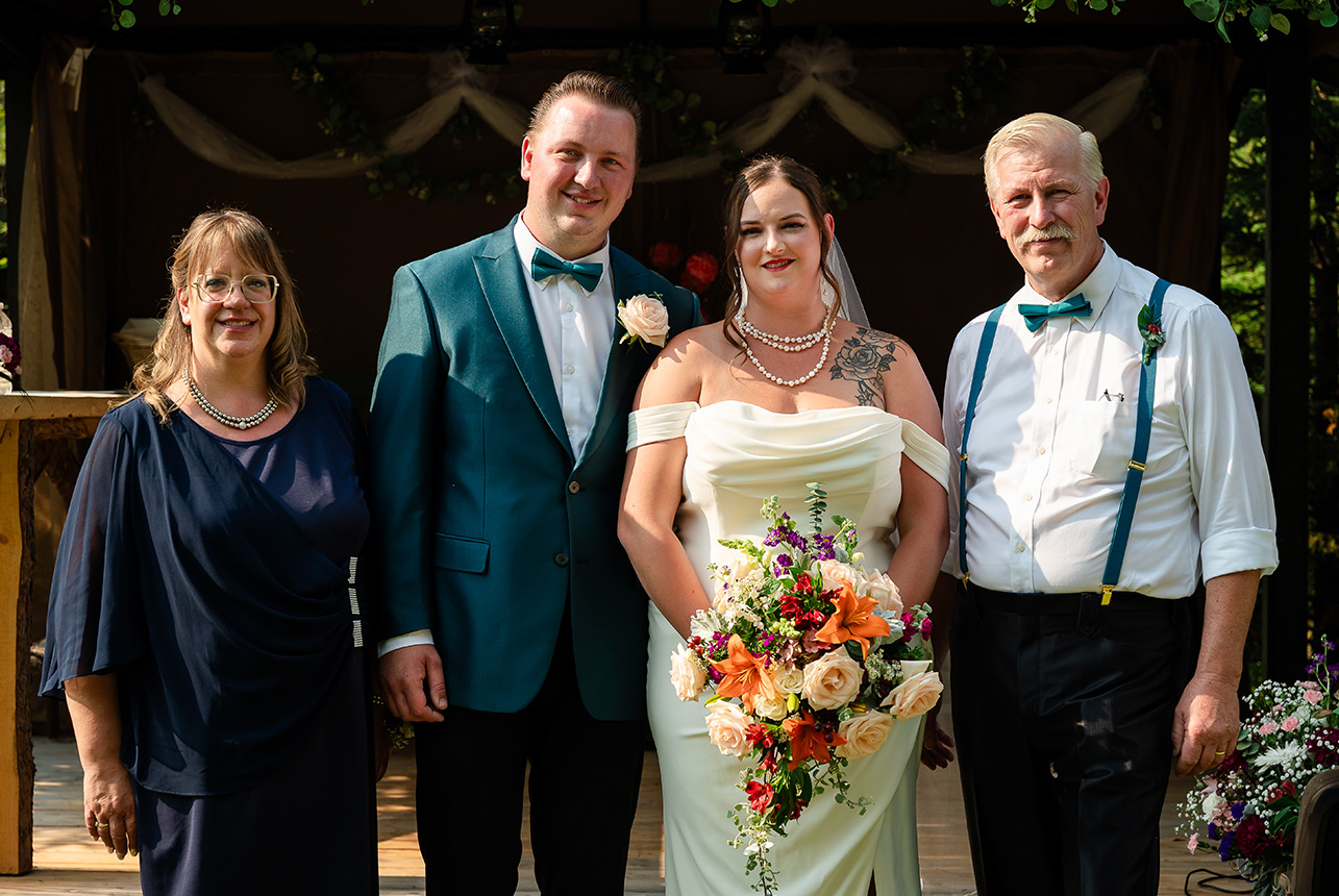 Bride and groom pose with the groom’s parents, his father also serving as his best man, in a heartfelt wedding portrait