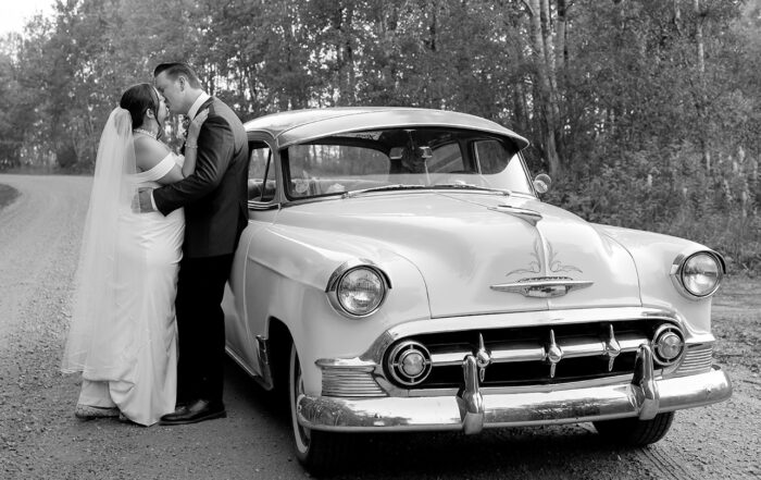 In a timeless black-and-white moment, the newlyweds share a romantic kiss on a curved gravel road, surrounded by the peaceful countryside