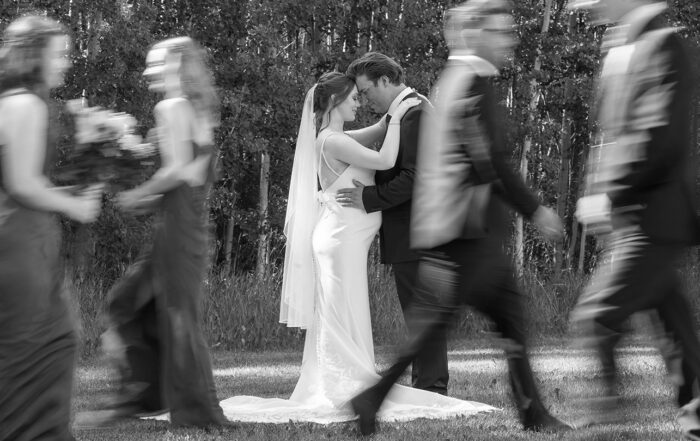 Bride and groom share a quiet moment as wedding party walks past in motion blur