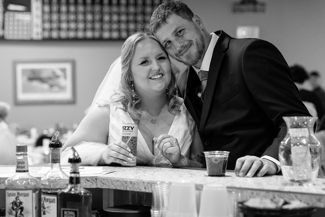 Bride and groom pose for a classic wedding photo while sitting together at the bar inside the Royal Canadian Legion