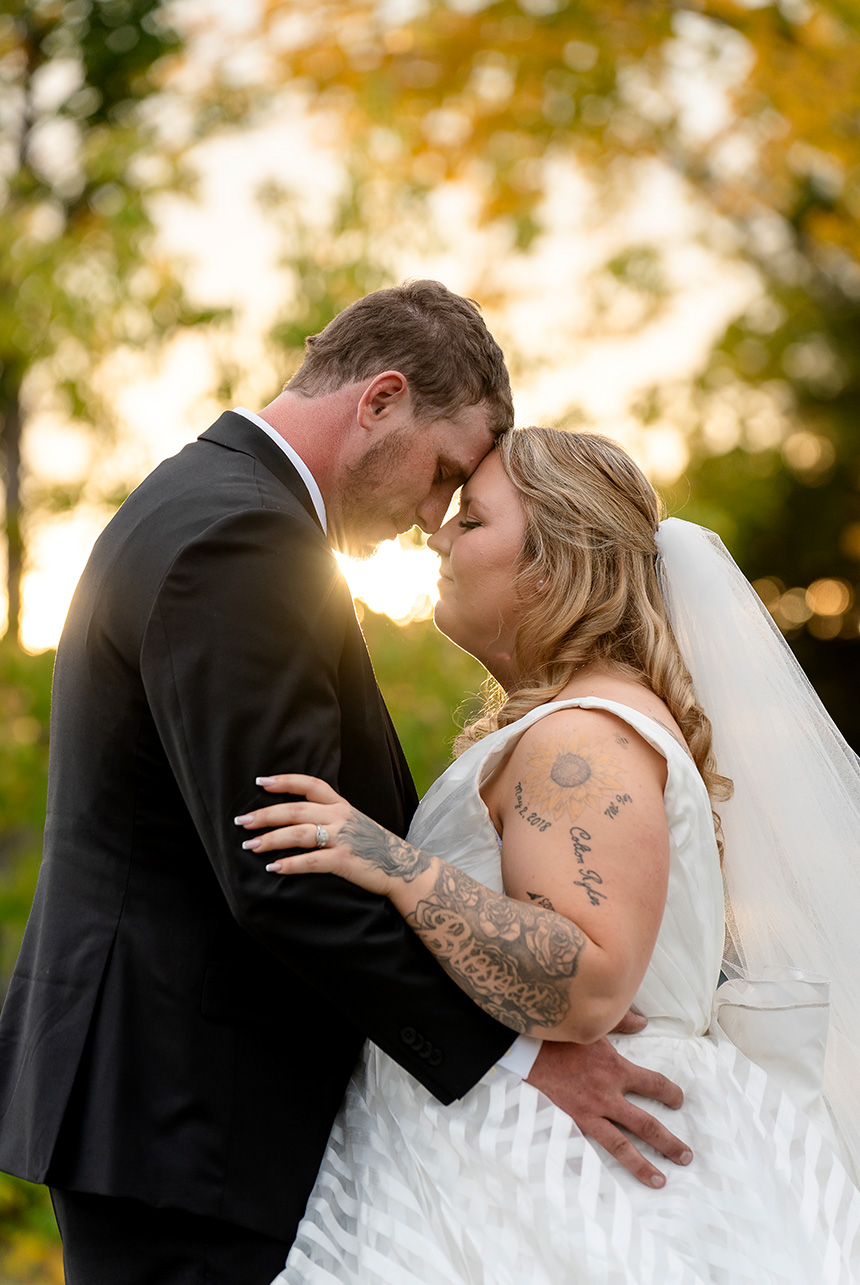 Bride and groom embrace head-to-head as the autumn sunset glows under their chins