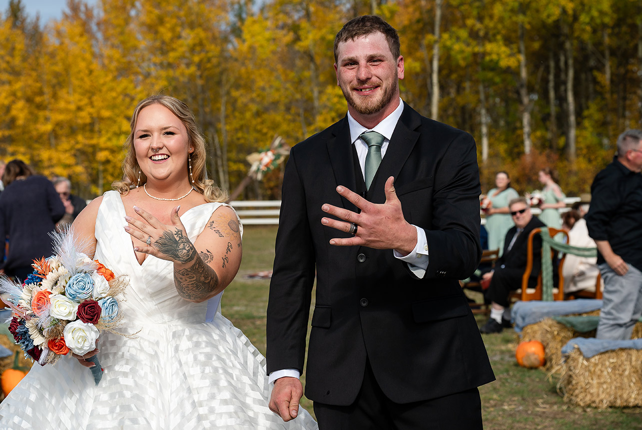 Bride and groom walk up the aisle, showing off their wedding rings as the wedding party celebrates with them at Finnegan Farms