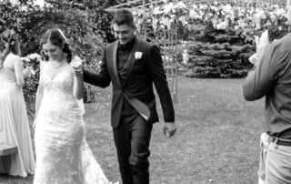 Black and white wedding photo of Juan and Hope walking hand in hand down the aisle at Greenland Botanic Gardens in Sherwood Park, near Edmonton, smiling with accomplishment and surrounded by small bubbles.
