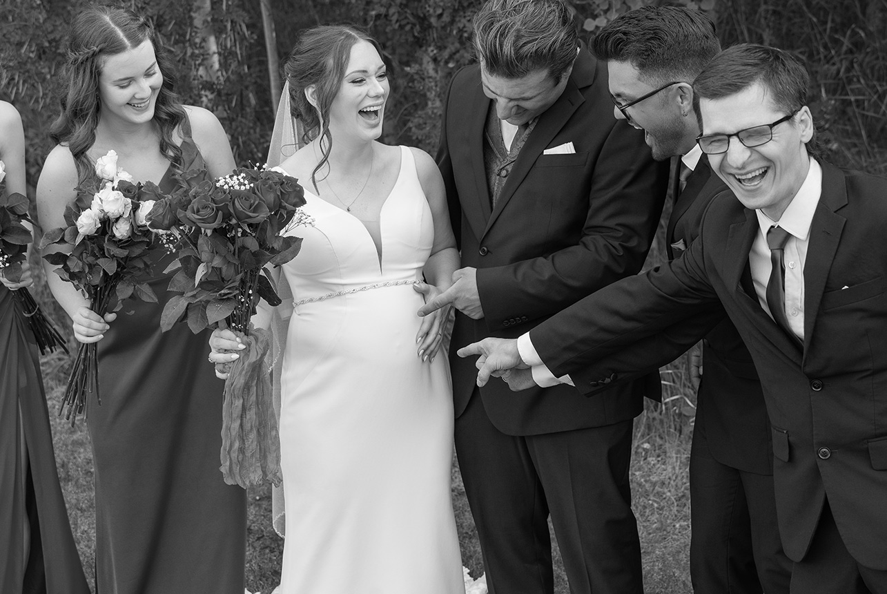 Bride and groom laughing with wedding party during candid group photo
