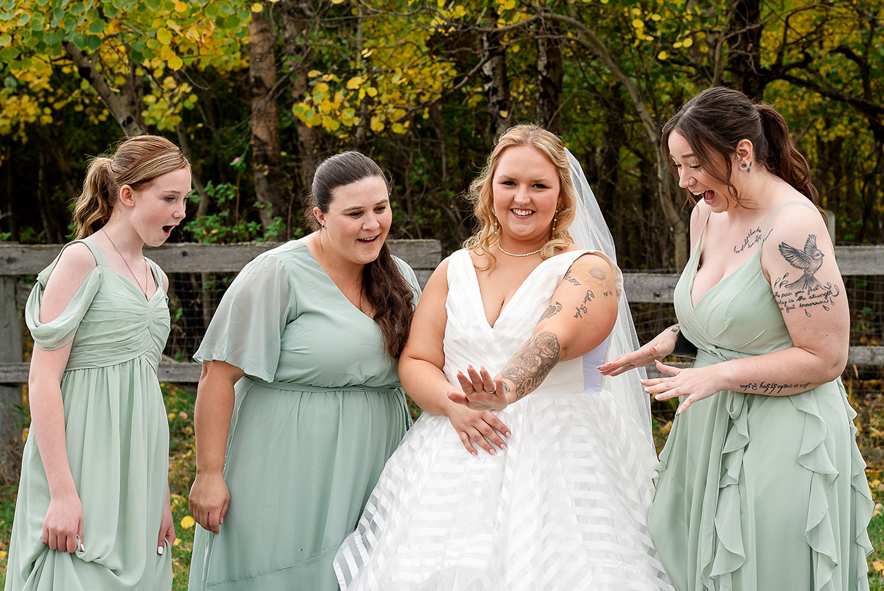 Bride shows off her ring as bridesmaids look on in awe and excitement against an autumn backdrop
