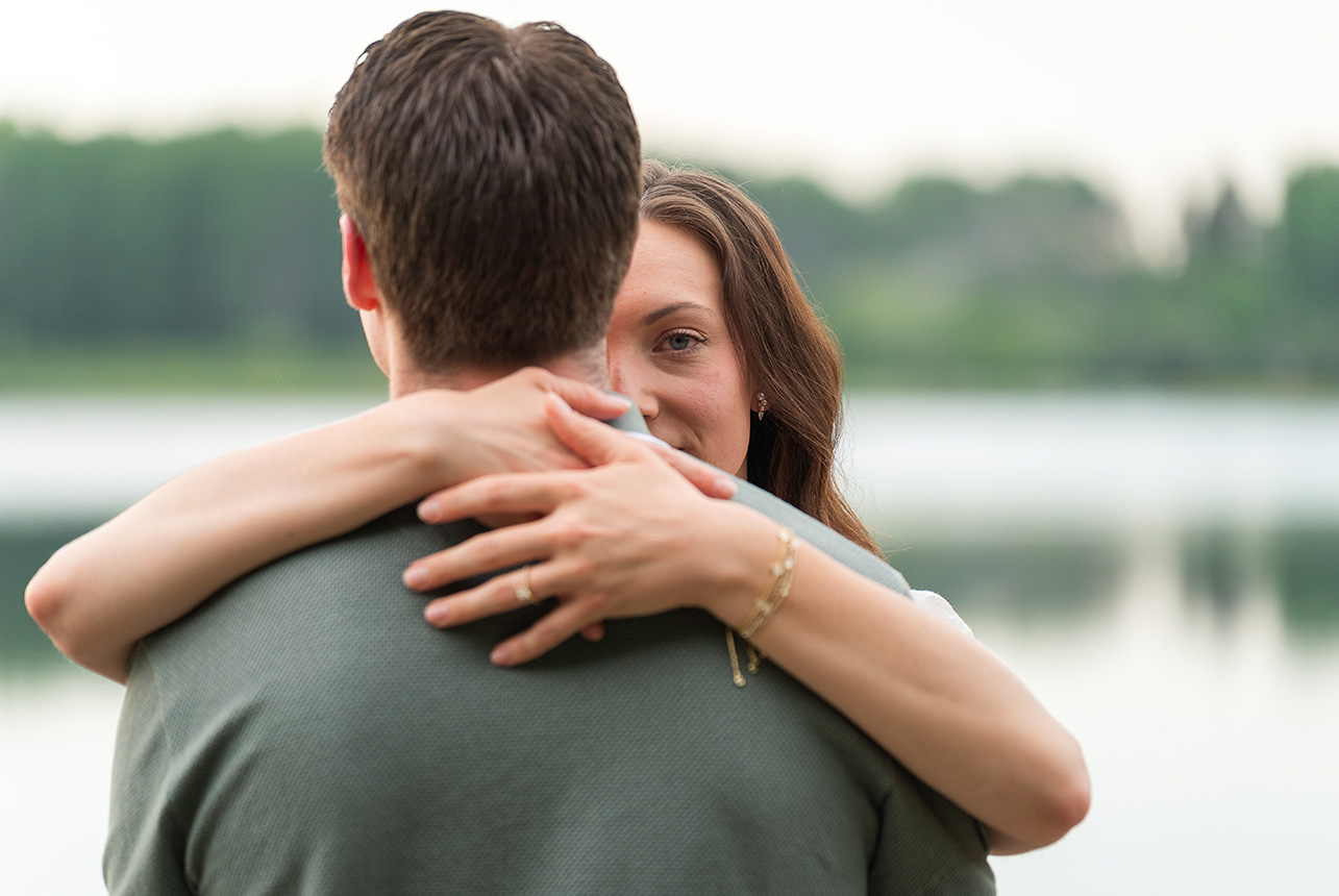 bride to be gazing over fiancé shoulder Woman embraces her fiancé at the lake, gazing warmly over his shoulder with a soft smile