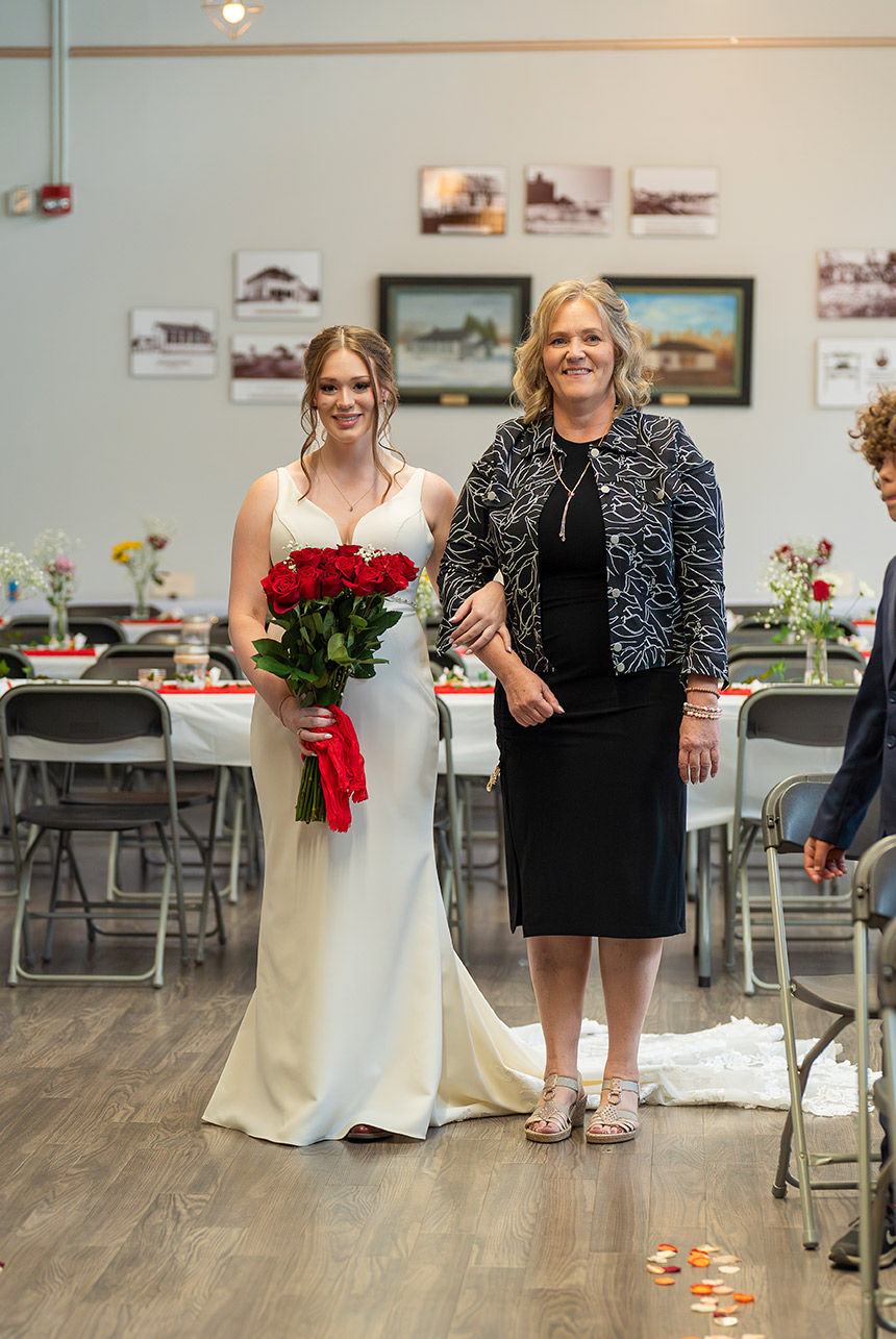 Bride walking down the aisle with her mother holding bouquet of red roses