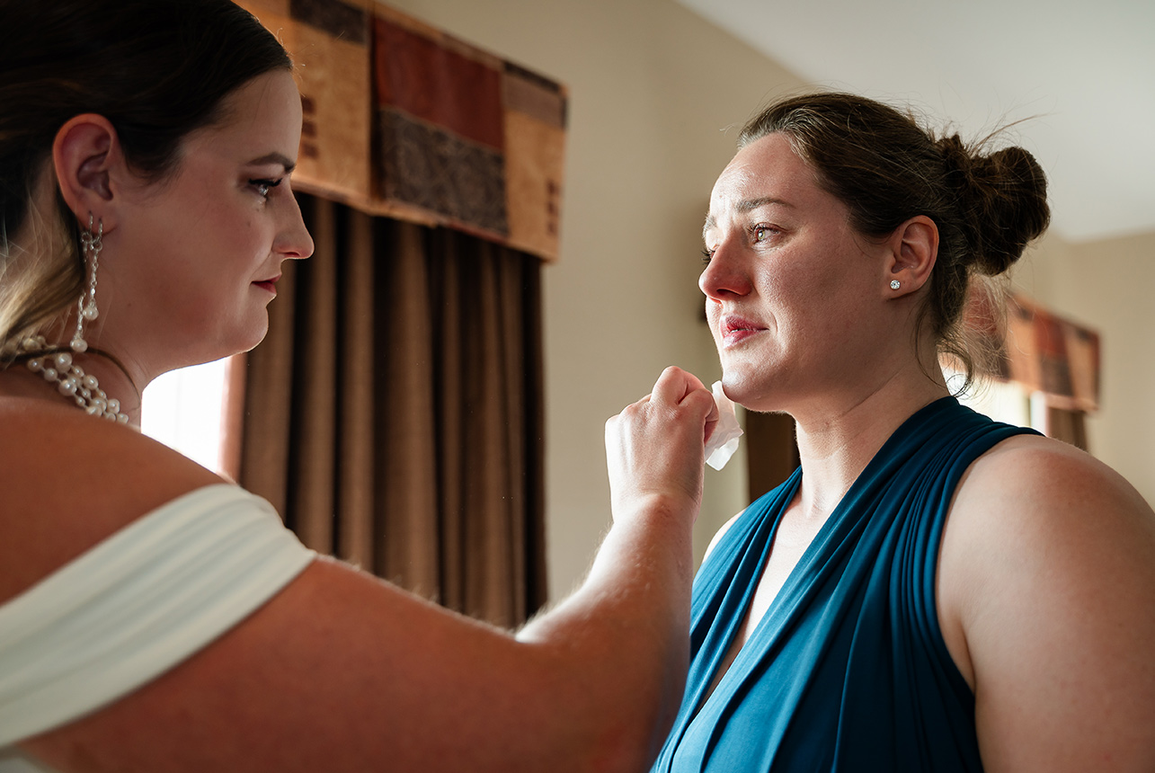 Bride gently wipes away her sister’s tears, sharing an emotional moment before the wedding ceremony begins