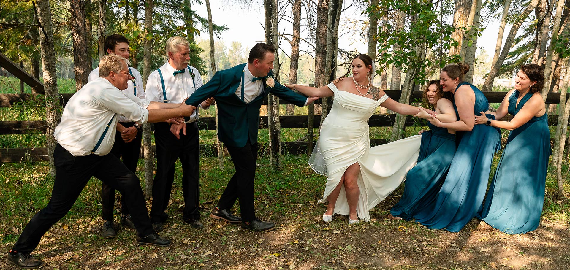 Bridesmaids playfully pull the bride away from the groom as the groomsmen try to hold onto him in a fun wedding party pose