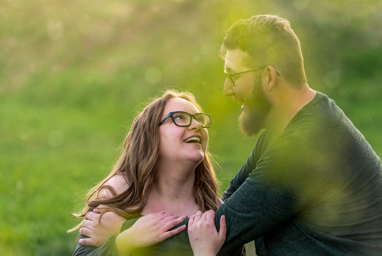 Couple laughing together in a soft spring meadow, surrounded by fresh greenery and dreamy evening light