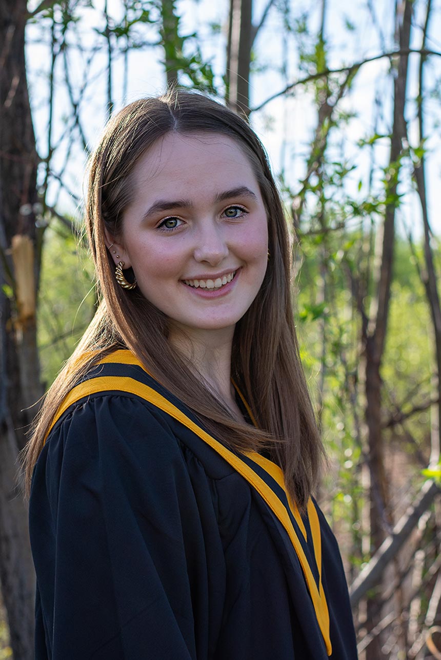 Young woman in Matte Navy Blue graduation gown and yellow school colors stole, turning to the side with a bright smile and a gaze that speaks of her accomplishments