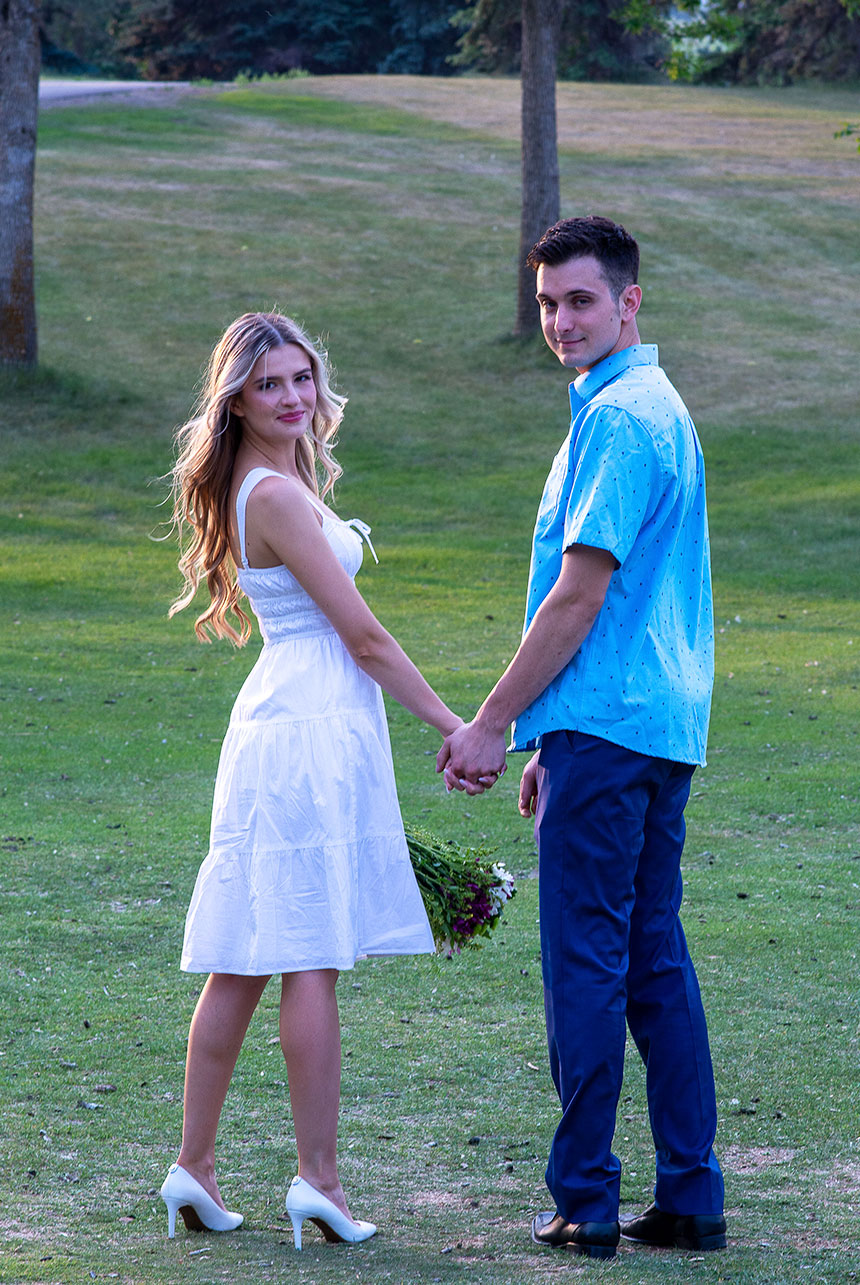 Couple holding hands and looking back, with the woman in a flowing dress and heels, holding a bouquet