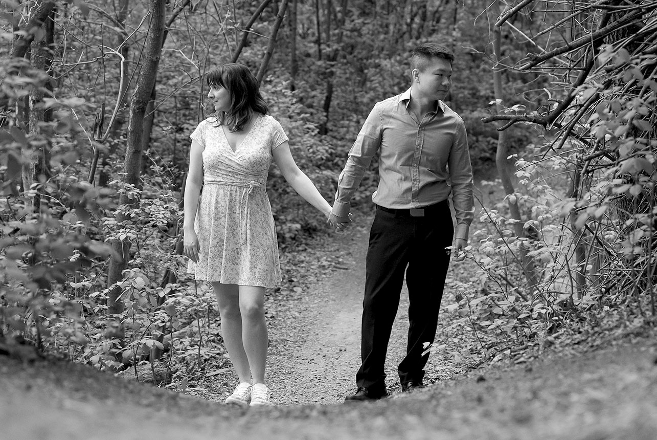couple holding hands forest black white Black and white photo of engaged couple walking hand in hand down a quiet forest trail in Edmonton