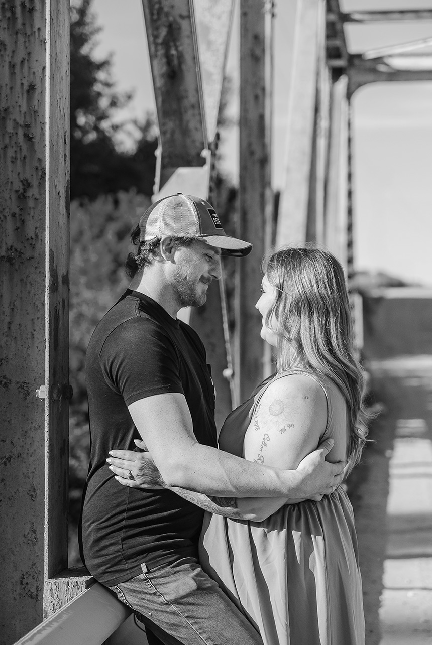 Couple sharing an intimate moment on a weathered steel bridge, sunlight softening the rusted metal