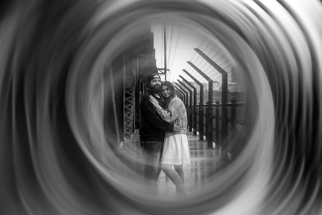 Unique black and white engagement photo through ring framing on Edmonton bridge