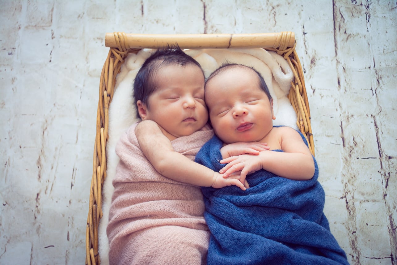 Two newborn cousins sleeping together in a basket during a professional studio newborn photography session.