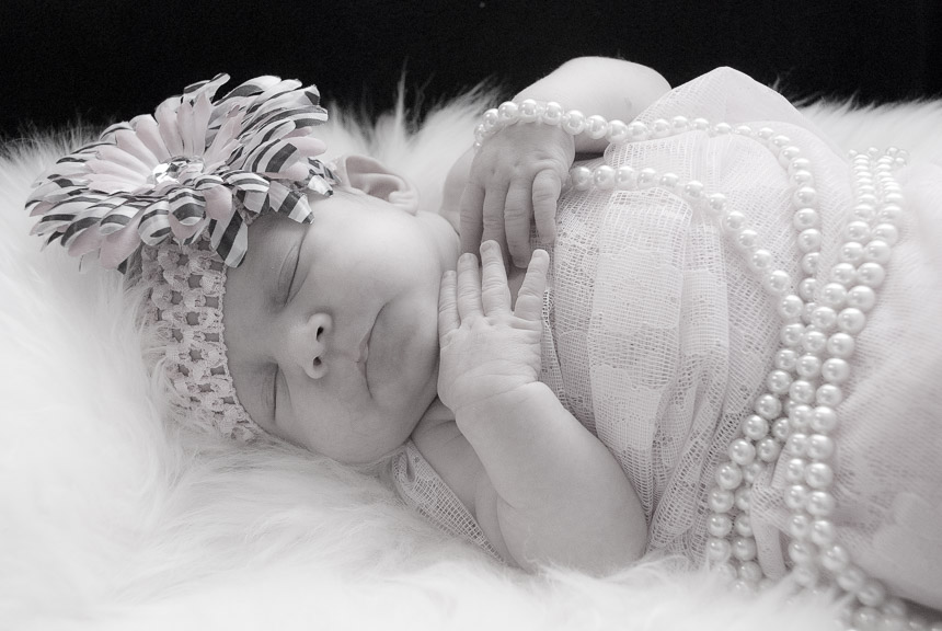 Sweet newborn baby girl holding pearls while sleeping soundly in a delicate dress