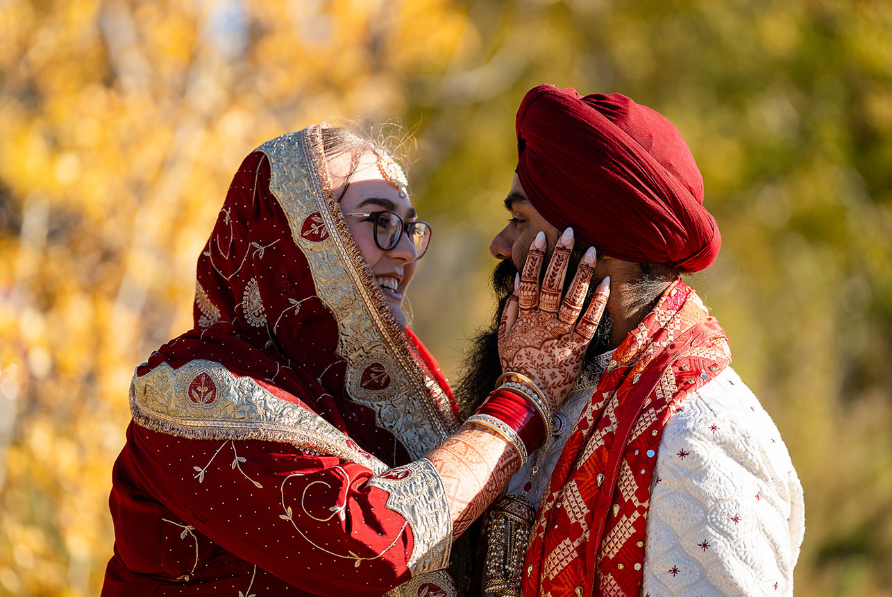 Henna-adorned hand cupping the groom’s face; rich red and gold attire and warm smiles