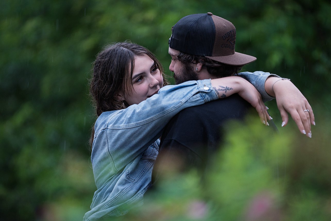 Couple hugging during a rainy engagement session along Edmonton’s river valley near the Muttart Conservatory