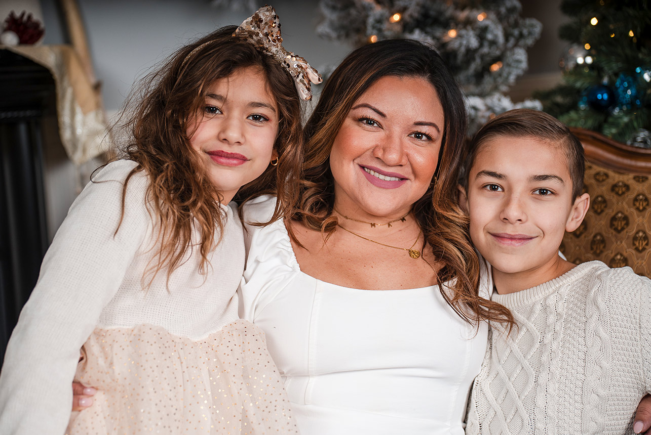 Mother with two children smiling close together in a festive studio by the Christmas tree.