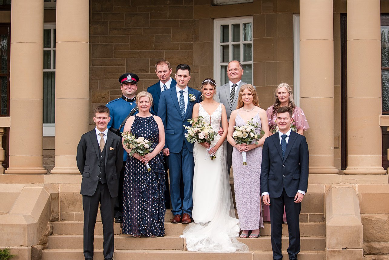 Formal family wedding portrait on the stone steps of Government House in Edmonton, with the bride and groom centered and relatives arranged in two rows