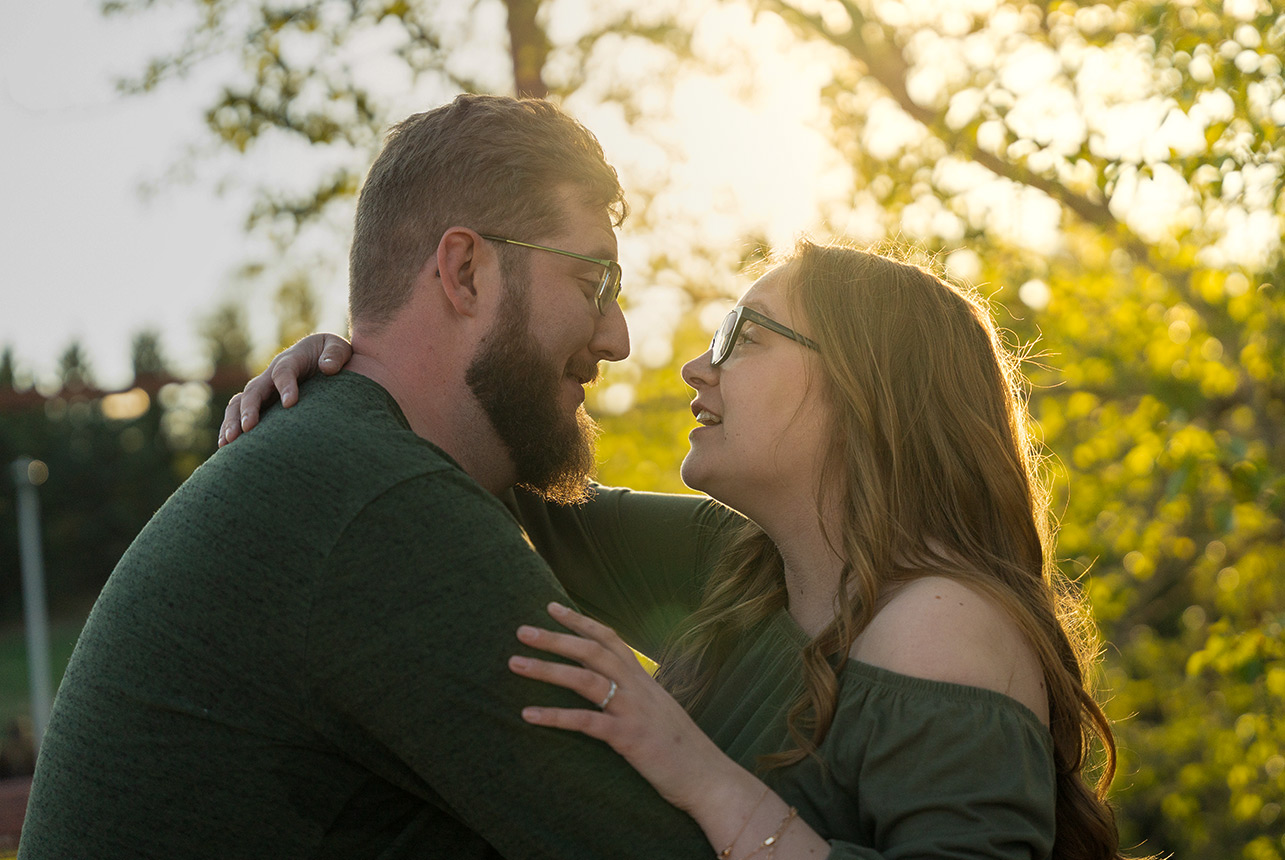 golden hour close up couple smiling eyes Couple smiling at each other in soft evening light with spring trees in the background at Rundle Park