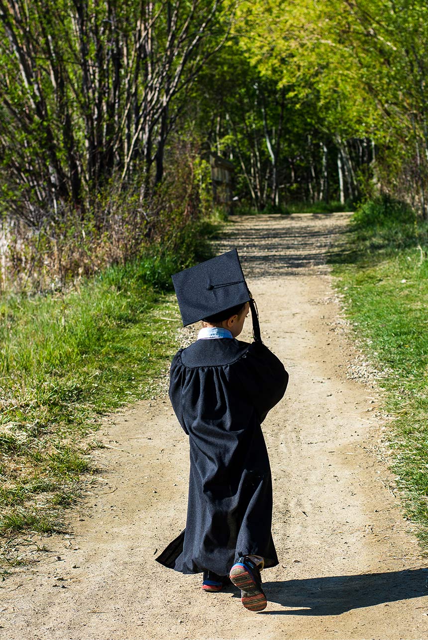Kindergarten graduate walking on dirt path in cap and gown