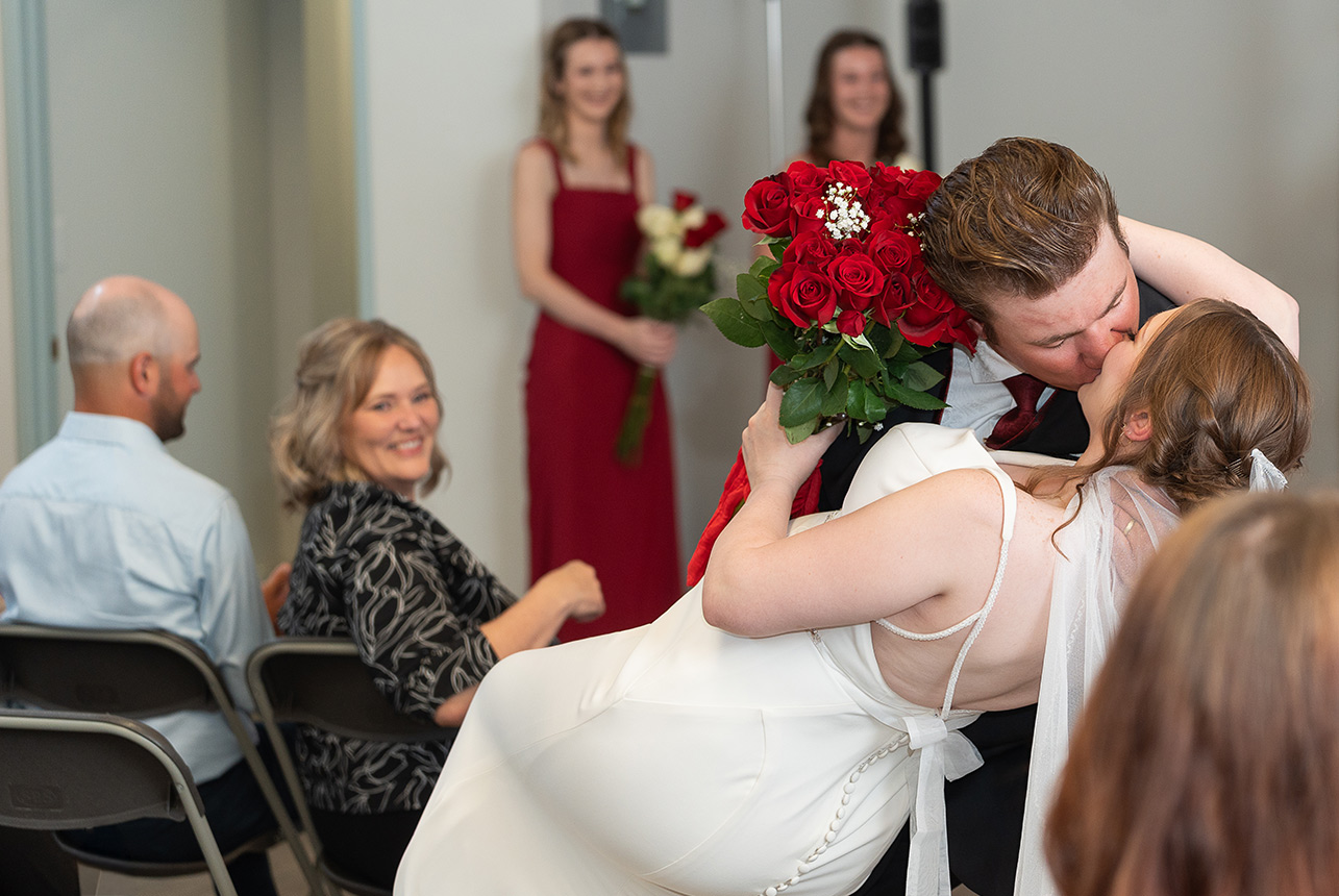 Groom dips bride for a kiss while holding bouquet of red roses