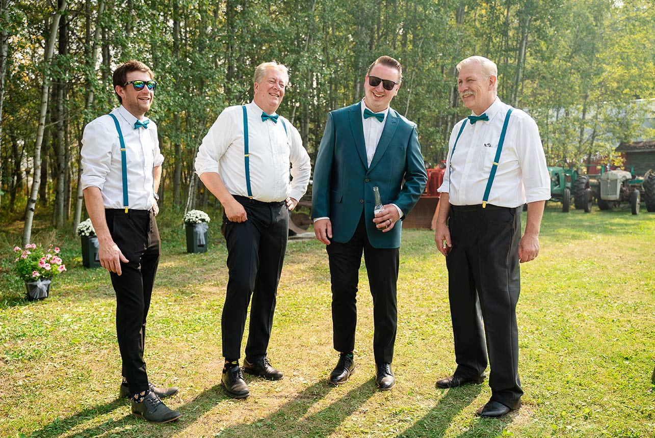 Groom and groomsmen, dressed and ready, enjoy a beer in the acreage yard, with antique tractors and trees in the background