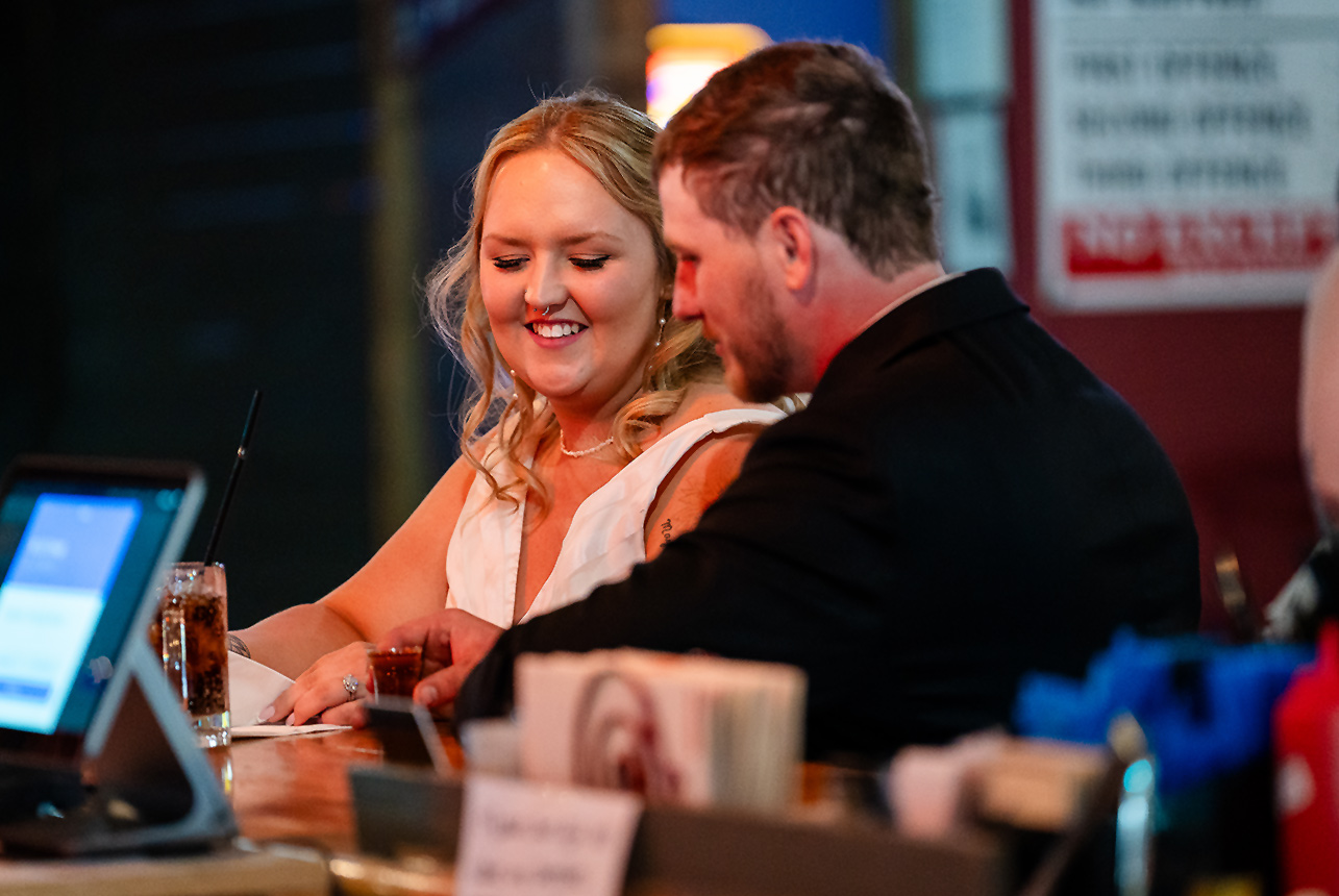 Side view of the groom reaching for a drink at Kicks Saloon Bar as the bride looks down at the glass
