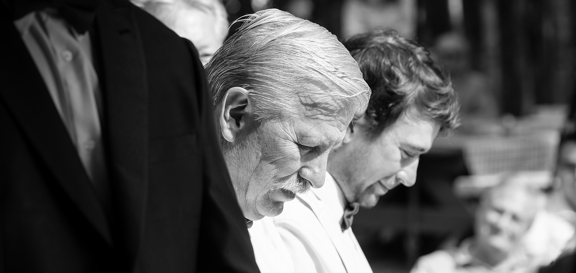 Two groomsmen stand with heads bowed and eyes closed, lost in the emotional words of the wedding ceremony