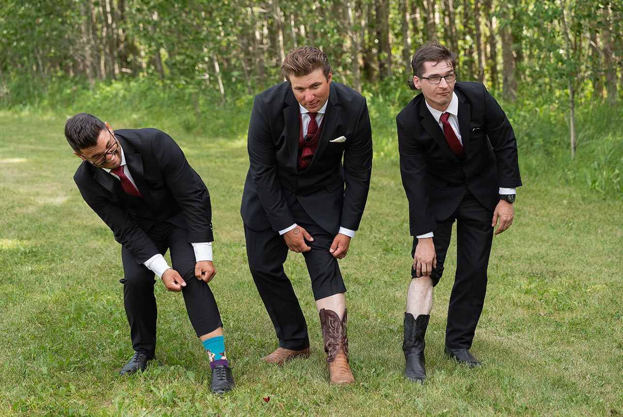 Groomsmen showing off colourful socks and cowboy boots at outdoor wedding