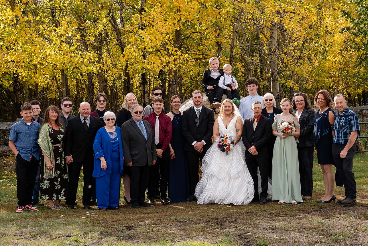Large family group photo with the bride and groom, their two boys sitting on a haybale, and autumn colors in the background
