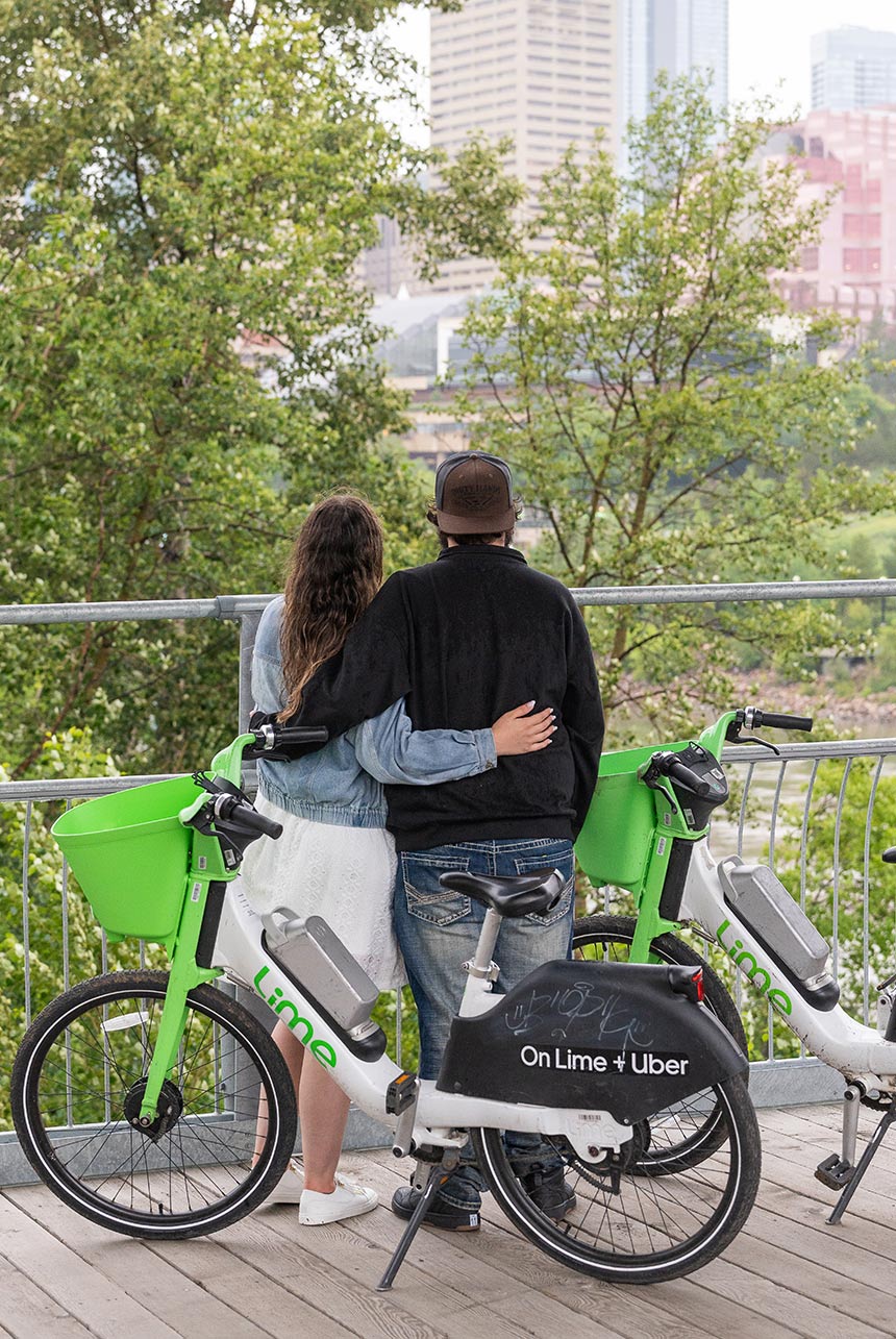 Couple stands arm-in-arm beside Lime bikes overlooking downtown Edmonton