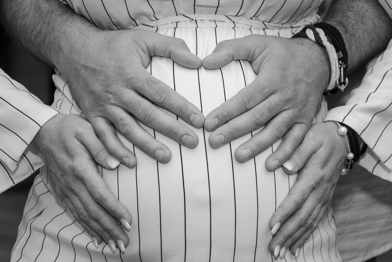 Couple's hands cradle maternity belly in a heart shape" to describe the image in a poetic and emotional tone.