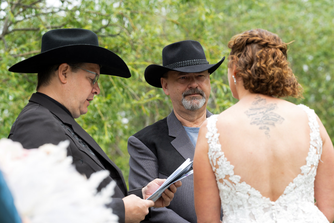 Outdoor wedding ceremony with officiant and groom wearing black cowboy hats
