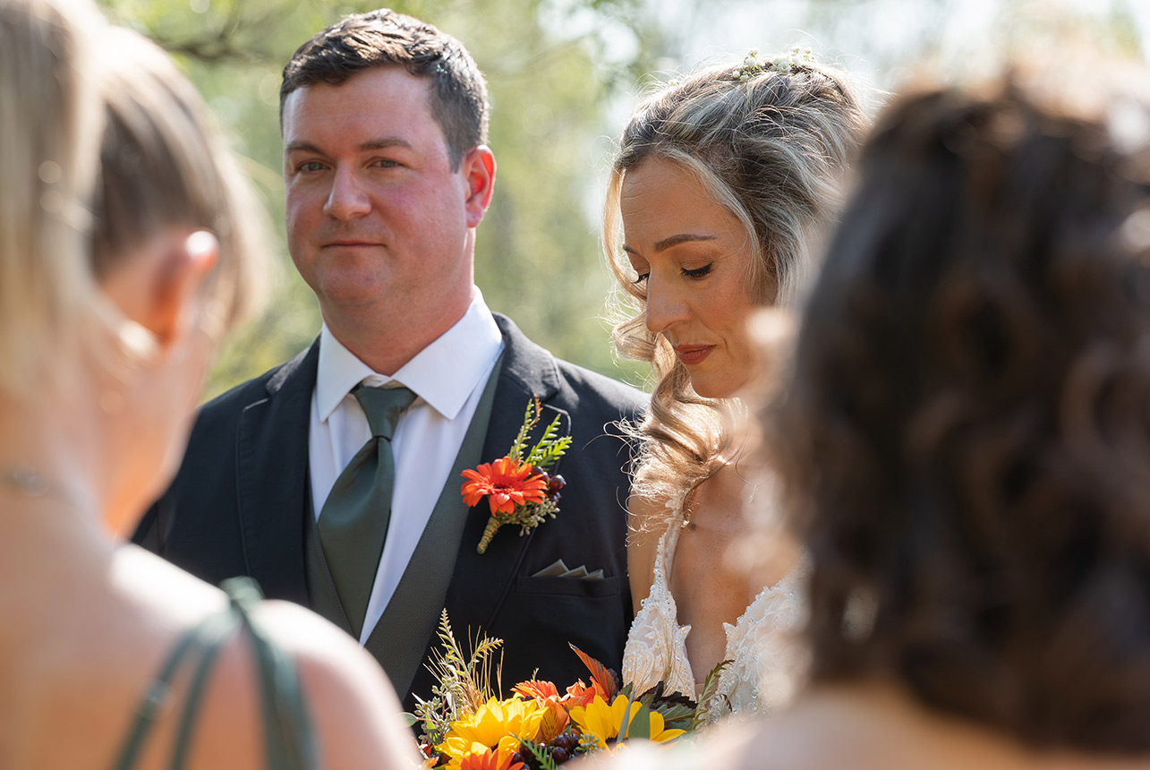 During the vows, the couple hold hands and listen, softly framed by guests in the foreground