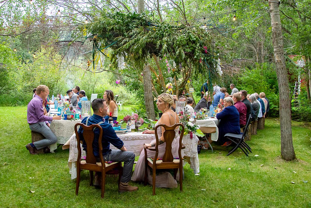 Rustic backyard wedding reception with long farm tables and greenery