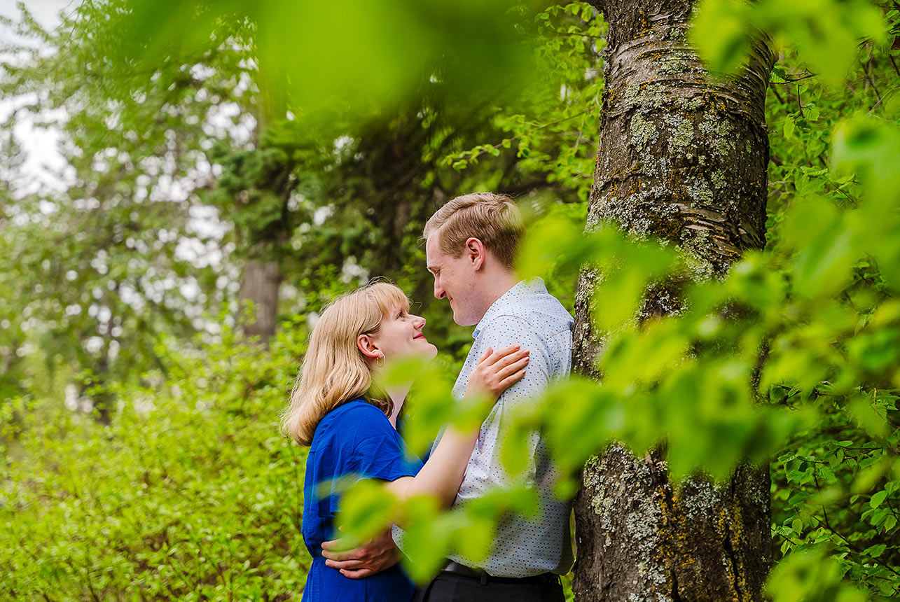 sherwood park engagement couple hug framed by green leaves review Engagement couple hugging by a tree, smiling at each other and framed by fresh green leaves in Sherwood Park