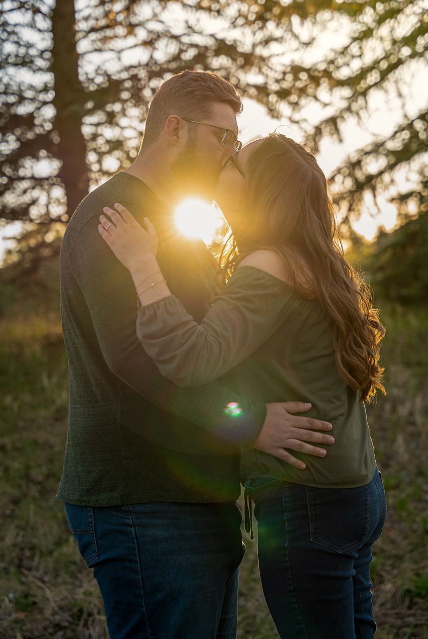 Sunlight meets soulmates—Catriona Hope Photography captures this golden moment full of promise, joy, and love Couple kissing as the sun sets behind them in a forest clearing during their golden hour engagement session in Rundle Park, Edmonton