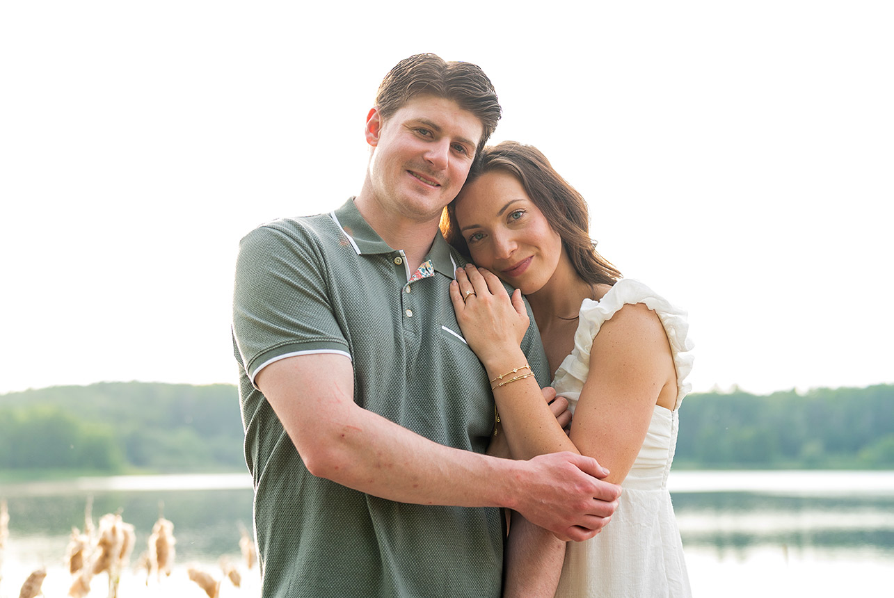 sunlit embrace golden hour engagement lake Couple stands by the lake, eyes closed and smiling in a soft golden hour embrace