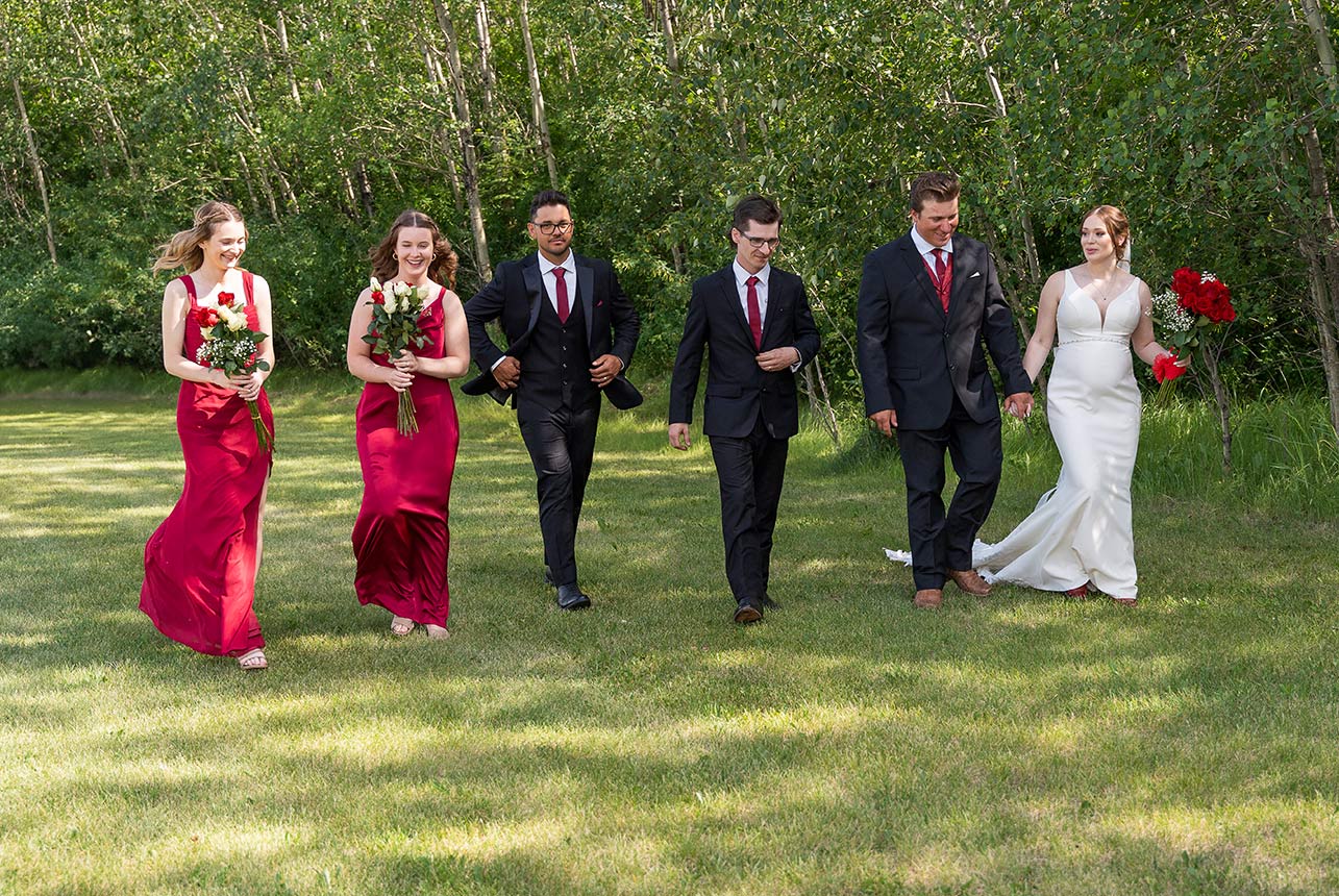 Bride and groom walking with wedding party across sunny lawn