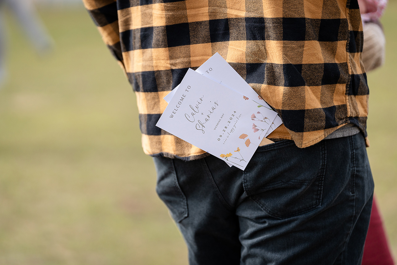 Wedding program tucked into the back pocket of a man in blue jeans and flannel shirt